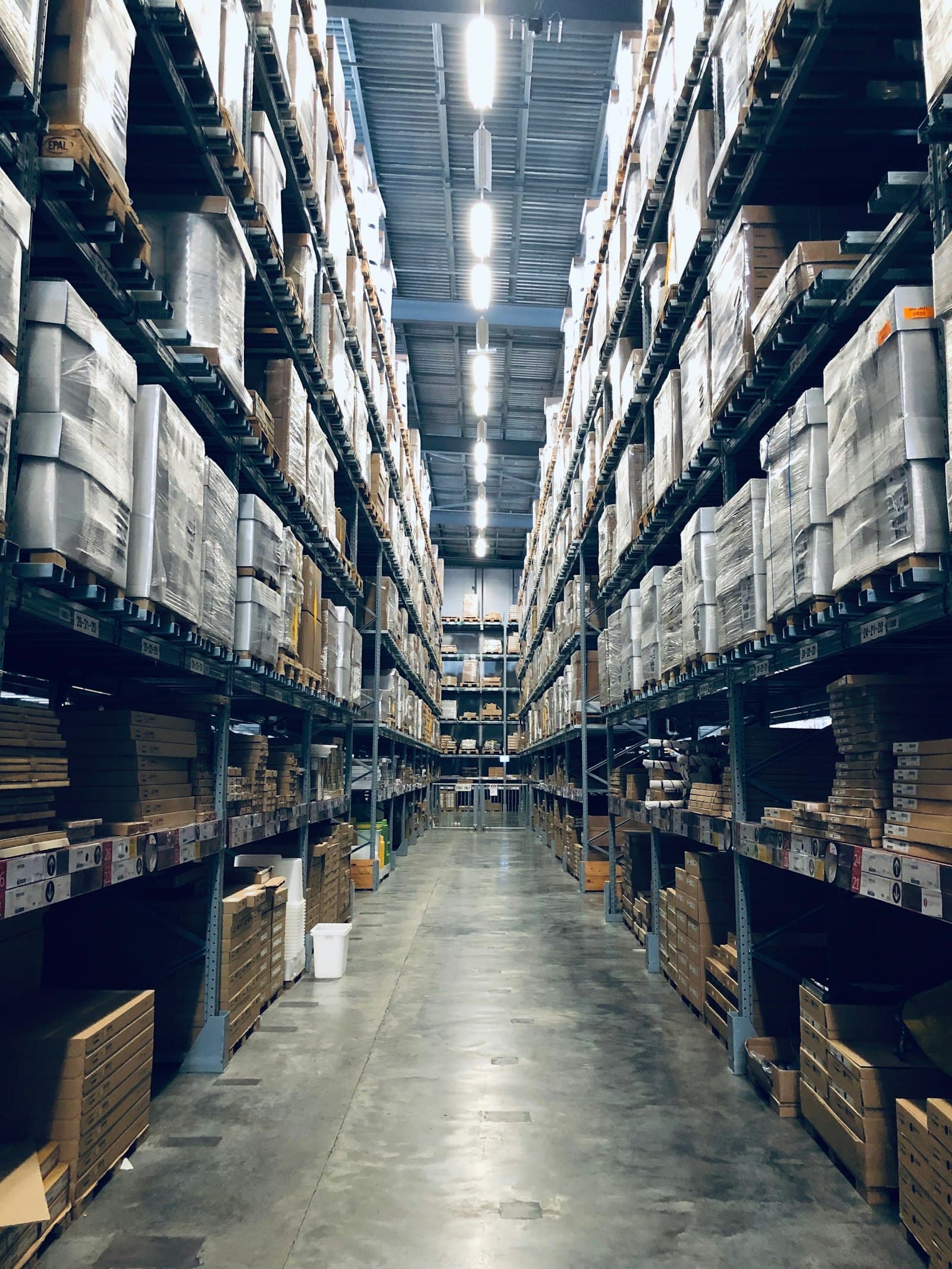 Pasillo de bodega con tarimas y cajas en anaqueles altos