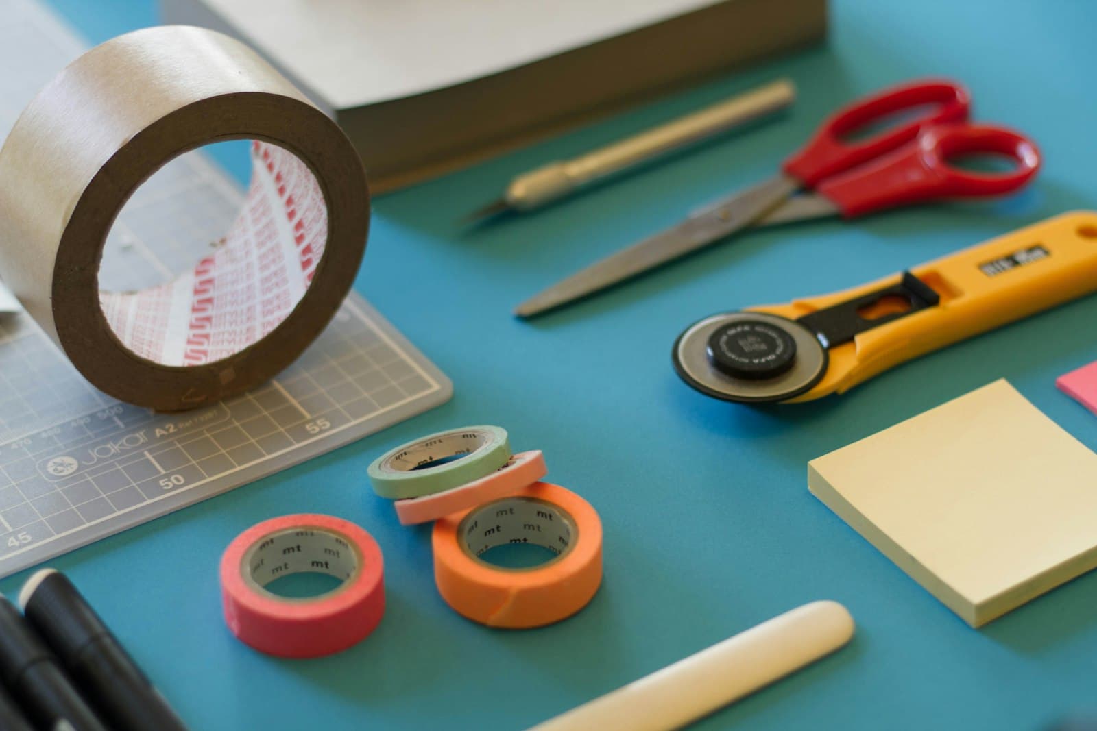 Cinta, tijeras, cúter y hojas sobre una mesa de papelería